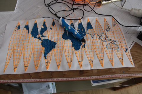 A 3D pen on a world-map study made from blue and yellow filament, photographed in 2016
